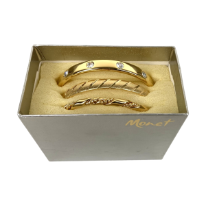 Drie goudkleurige bangle armbanden van Monet, waarvan één versierd met strass-steentjes. De armbanden hebben een diameter van 7 centimeter en breedtes van respectievelijk 8, 7 en 4 millimeter. Elke armband is voorzien van een merk. De armbanden zijn nieuw en worden geleverd in hun originele doosje.