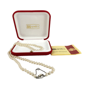 Ivoorkleurige handgeknoopte parelketting van Majolica (Spanje). Stijl: Avantgarde (Jaren '50). Met fraai sterling zilveren (925) slotje met twee kleine pareltjes en veiligheidskettinkje. Lengte: 70 cm. Diameter parels: 5 mm. Met bijbehorende rode doos en certificaat van echtheid. In prachtige glanzende staat.