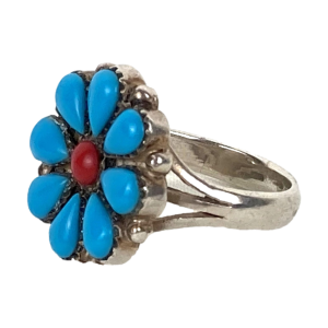 Zilveren Navajo cluster ring met rondom 8 turkoois steentjes en één ronde koraal in het midden. Ringmaat: 19 mm. Breedte ring: 3 mm. Diameter bloem: 2 cm. Gewicht: 7,8 gram. Gemerkt met zwaardje. In goede staat.