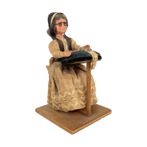 Vintage folkloristisch popje van een kantklossende oude dame zittend op een stoeltje. Hoog: 13 cm. Houten standaardje: 7x7 cm. Handgemaakt.